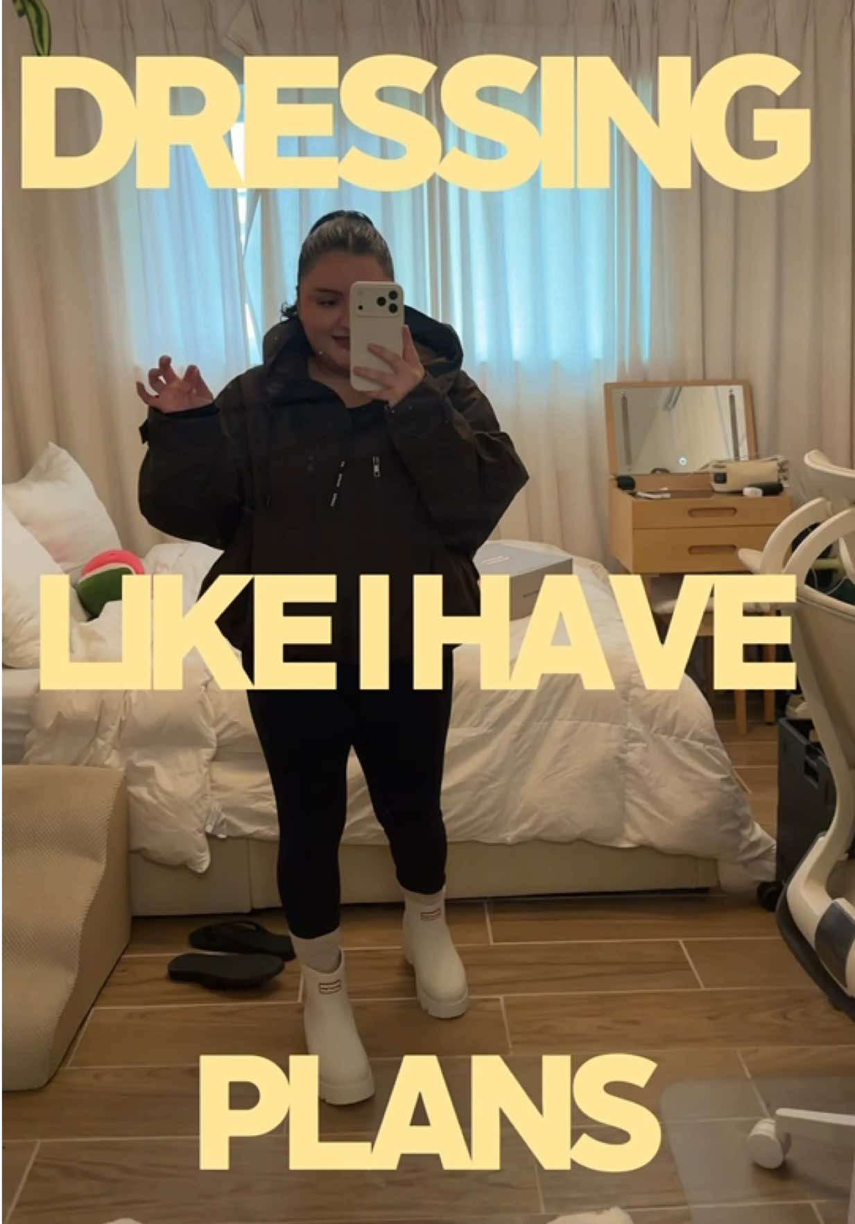 mirror selfie of mandy in a dark rain jacket, black leggings and white rain boots, with the words "dressing like i have plans" in big butter-yellow letters
